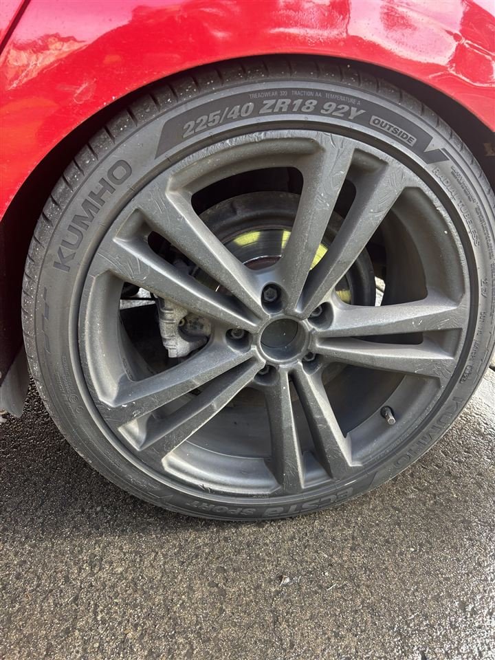 Grey alloy wheel with a dirty, rusty unpainted brake caliper before painting